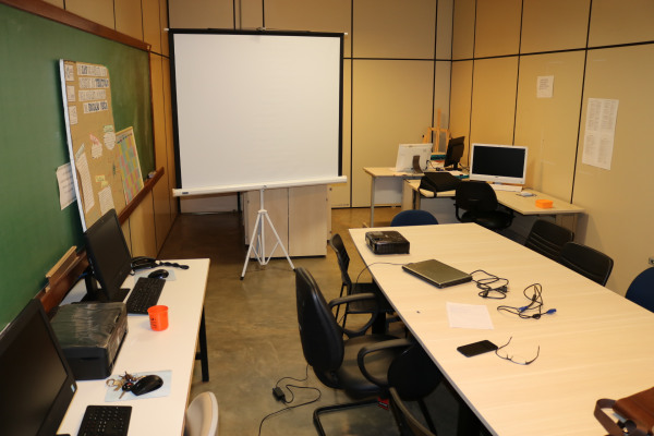 Sala com mesa de reunião, mesas de trabalho e 5 computadores